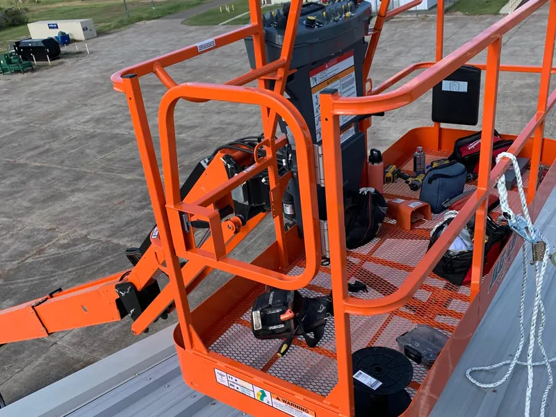 An orange articulating boom lift positioned on a metal roof, used to reach the ridge during a coating job