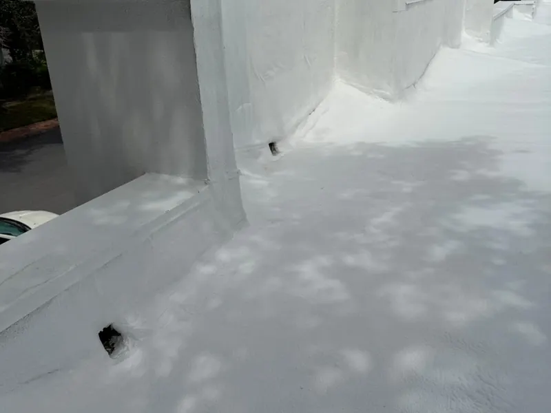 White coated parapet walls stepping across a flat roof, the coating carried seamlessly up the vertical faces