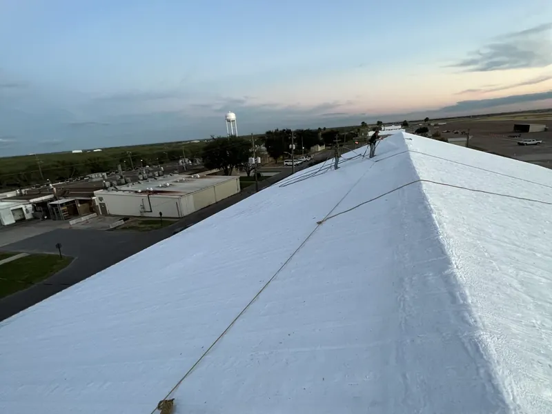 A freshly coated white roof ridge running toward the horizon at dusk, the surrounding site lit by low evening light