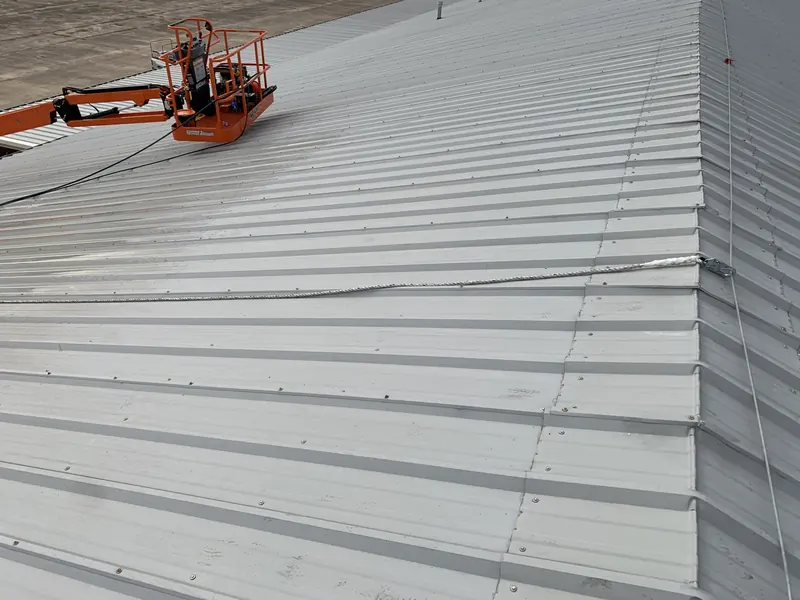 The coated edge of a metal building wall and roof, with an orange scissor lift positioned on the roof deck behind it
