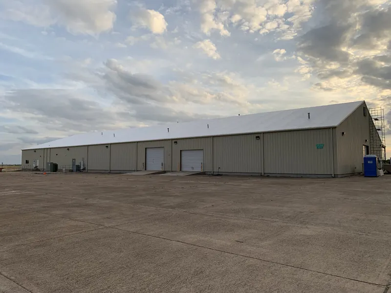 A long tan metal warehouse building under a broad cloudy sky, one of the commercial properties insulated by Panda Insulation