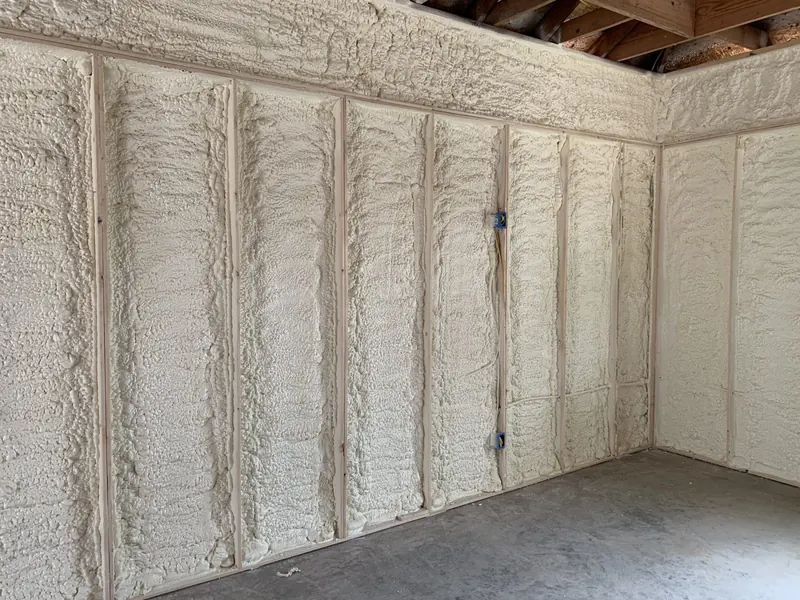 A finished interior wall with every stud bay filled flush with white open-cell spray foam, trimmed level with the framing