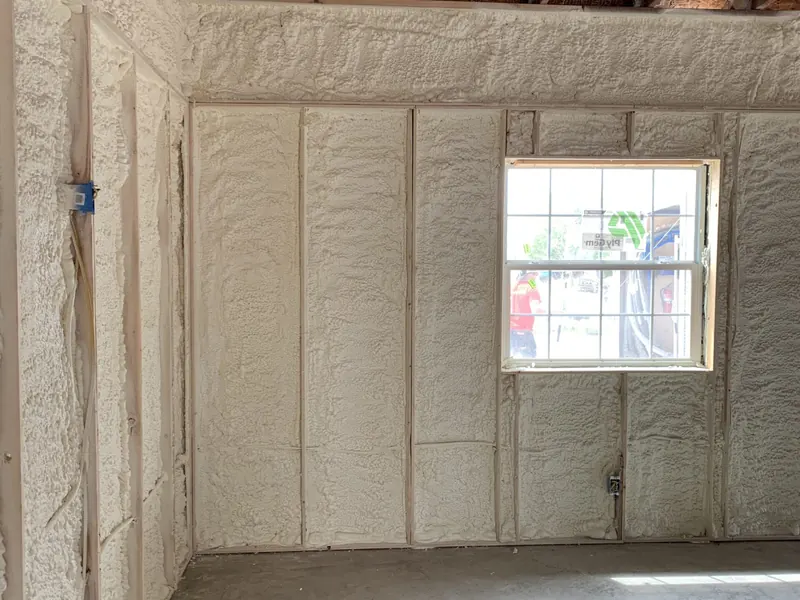 A small room insulated wall to wall with white spray foam, daylight coming through a single window in the far wall