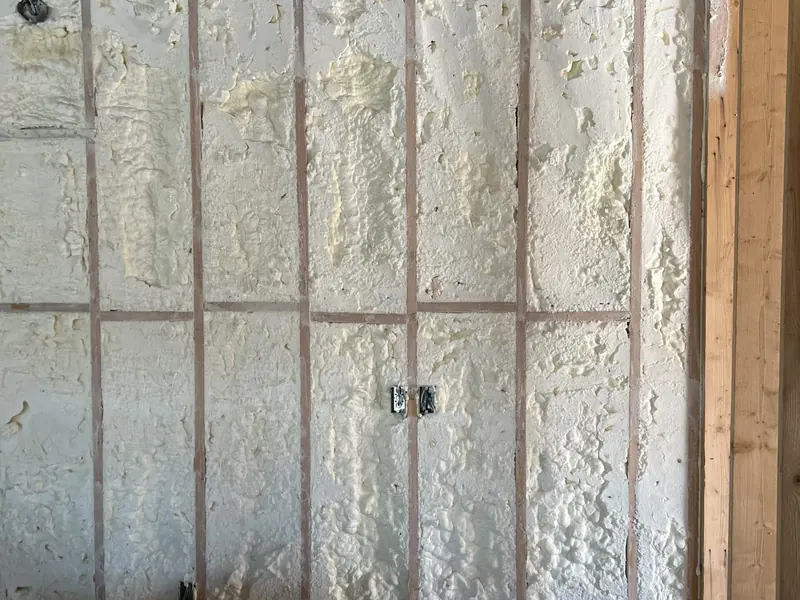 A detail view of a stud wall filled with open-cell spray foam, the foam shaved flush to the face of the studs