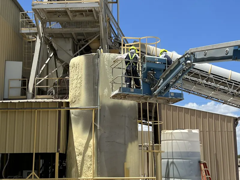 A cluster of large industrial process tanks and silos with conveyor structures, insulated and coated against the weather