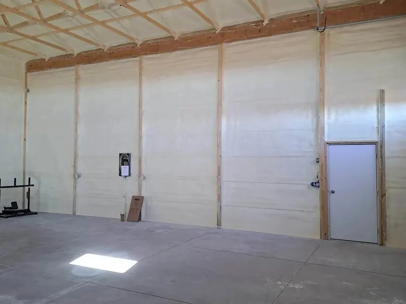 A completed metal building interior, walls and roof deck fully insulated in pale spray foam, floor swept clean