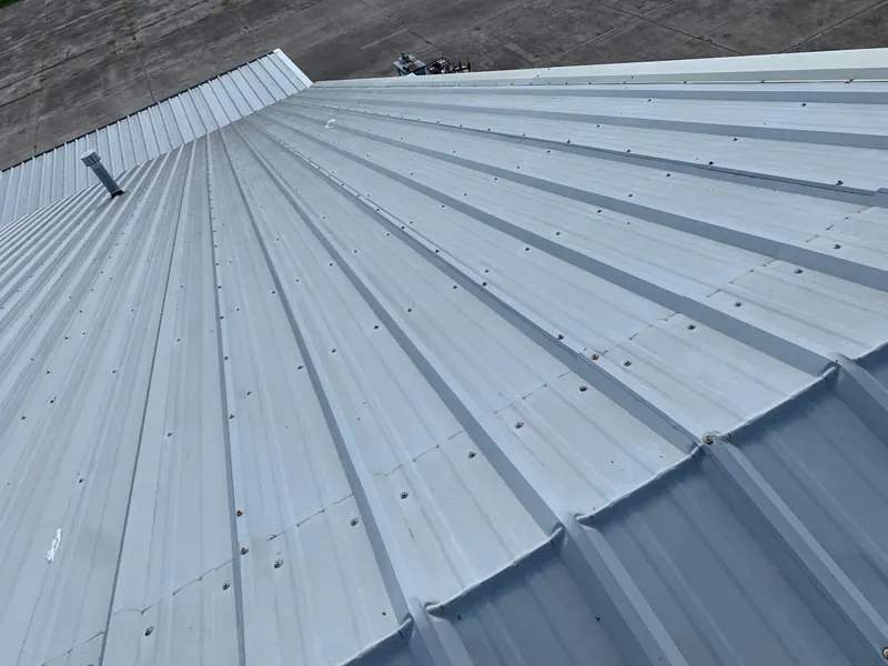A close overhead view of coated standing-seam metal roof panels, the ribs running in sharp parallel lines toward the ridge