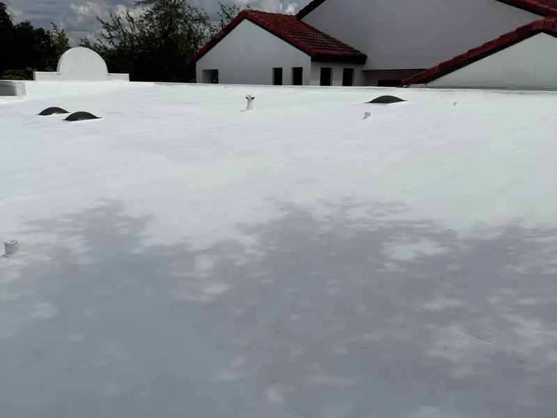 A completed white reflective roof coating across a low flat roof, with the red tile roof of the adjoining building behind