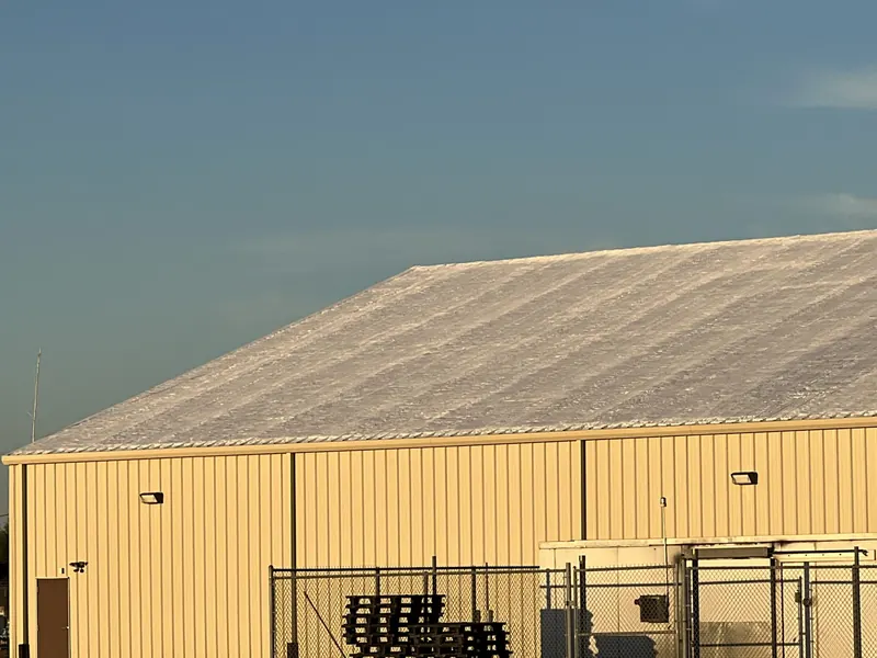 A yellow metal commercial building with its coated roof catching low golden evening light
